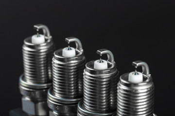 A set of new spark plugs of the car, and spare parts of vehicles on a dark background.