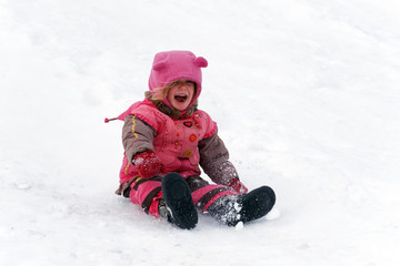 A three year old girl happy and laughing sliding in the snow in Canada