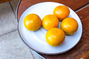 Oranges in white ceramic plate on wooden table 