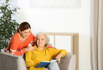 Elderly woman with female caregiver in living room. Space for text
