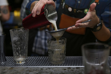 Bartender pouring tasty cocktail at counter in nightclub, closeup