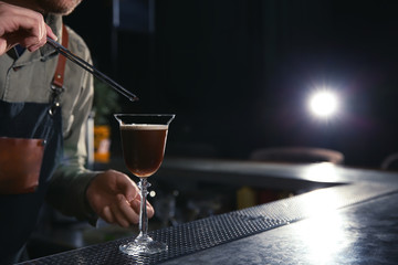 Fototapeta na wymiar Barman adding coffee bean to martini espresso cocktail at counter, closeup. Space for text