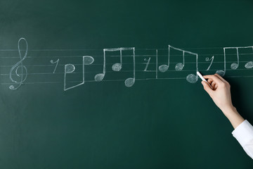 Woman writing music notes with chalk on blackboard, closeup