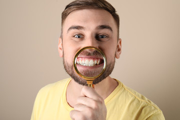 Young man with healthy teeth and magnifier on color background