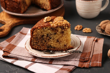 American homemade nutty cake is located on a dark background. Piece of cake in the foreground