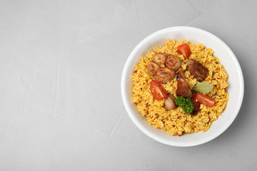 Bowl of delicious rice pilaf on grey background, top view with space for text