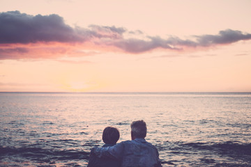 elderly couple sitting and hugging each other looking at the sea at sunset relaxing. Concept of...