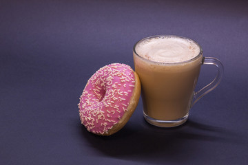 Transparent glass cup with coffee and pink donut on blue background. Bright tone, soft focus