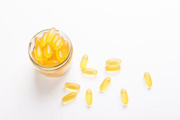 Omega 3 capsules in glass jar on white background Fish oil Yellow softgels Vitamin D, E, A supplement
