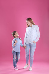 Happy woman and daughter in stylish clothes on color background