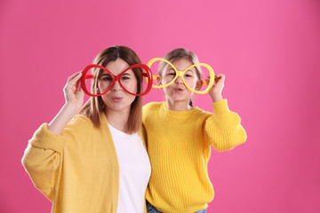 Happy woman and daughter with funny glasses on color background
