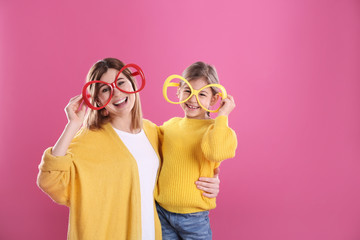 Happy woman and daughter with funny glasses on color background. Space for text