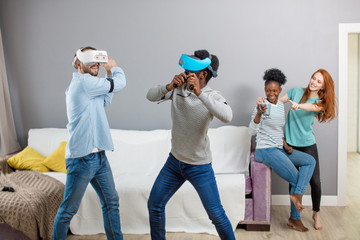 Group of multiracial male amd female students playing virtual game using vr goggles, having fun together ay home - Virtual omg reality and portable digital technologies