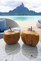 View of two fresh drinking coconuts on a table in front of the Mont Otemanu mountain in Bora Bora,...
