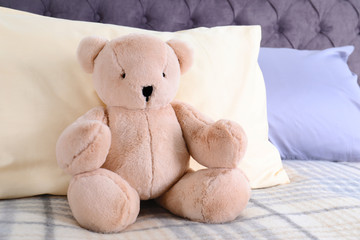 Cute teddy bear sitting on bed indoors. Space for text