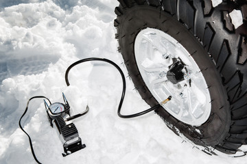 Checking tire pressure. Pumping air into auto wheel on the ATV 4wd quad bike stand in heavy snow. © Screaghin