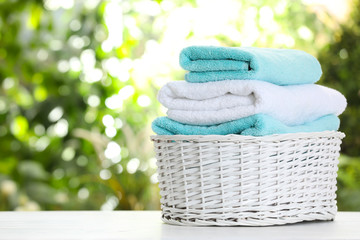 Basket with soft bath towels on table against blurred background. Space for text