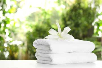Stack of clean soft towels and flower on table against blurred background. Space for text