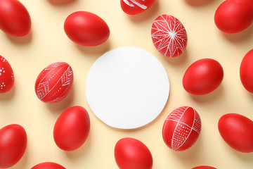 Flat lay composition of painted red Easter eggs and card on color background, space for text