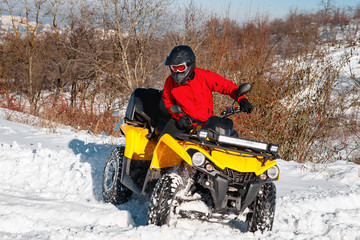 Fototapeta na wymiar Photo of young extremal driver in red warm winter clothes and black helmet jump in the air with the ATV 4wd quad bike stand in heavy snow with deep wheel track. Extreme moto winter sports.