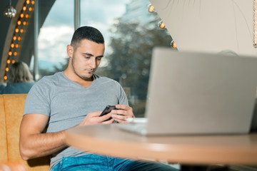 man works in a cafe. young guy looks into the smartphone.