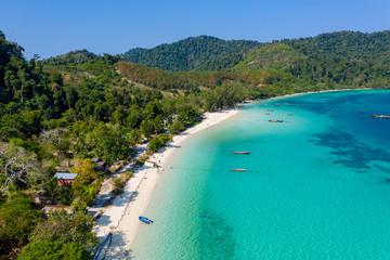 Aerial drone view of traditional fishing boats moored over a coral reef around a remote, green tropical island in the Mergui Archipelago