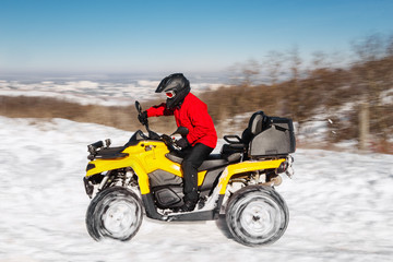 Fototapeta na wymiar Photo of young extremal driver in red warm winter clothes and black helmet drive his ATV 4wd quad bike stand in heavy snow with deep wheel track. Extreme moto winter sports.