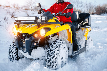 Close up photo of young man in red warm winter clothes and black helmet on the ATV 4wd quad bike stand in heavy snow with deep wheel track. Moto winter sports. © Screaghin