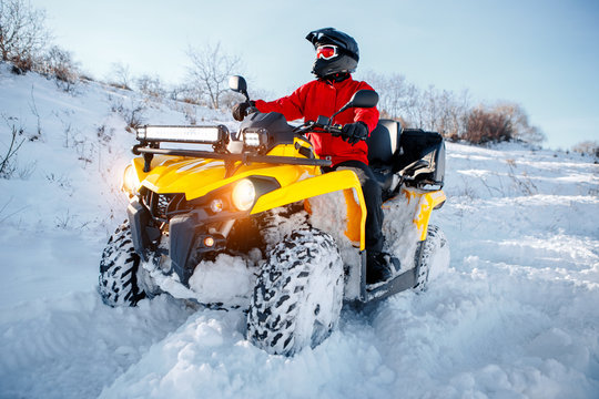 Young man driver in red warm winter clothes and black helmet on the ATV 4wd quad bike stand in heavy snow with deep wheel track. Moto winter sports.