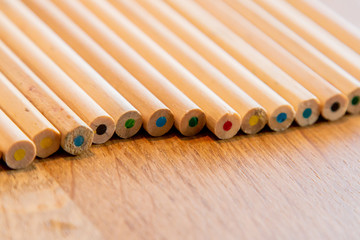 The ends of Various Coloured Pencil Crayons in a line on a wooden table