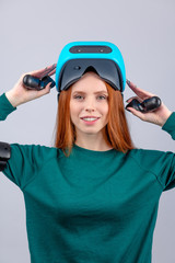 Active beautiful female player with long red hair , being excited watching virtual reality play with vr glasses on head, acting like an archer, aiming with virtual arrows