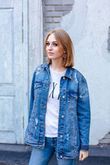 Fashion girl standing near brick wall in denim jacket and beautiful ear rings.