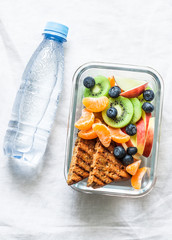 Healthy food snack sweet vitamin lunch box and bottle of clean water on a light background, top view. Peanut butter toast, apples, kiwi, tangerines, blueberry lunch box