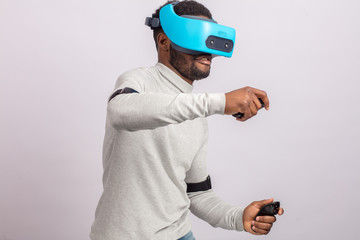 Dark skinned confident man with a short stubble, dressed in white pullower, wearing blue mobile virtual reality headset holding hands as if he is driving car isolated over white background.