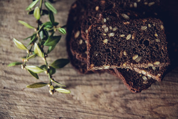 Close-up of the sliced brown bread at the cutting board on the wooden table with black background. Top view