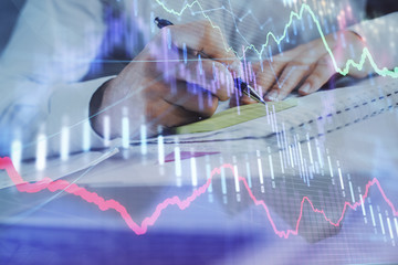 Close up of hands writing with double exposure of business charts. Financial concept.