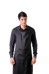 Fototapeta premium Young chef or waiter posing, wearing black apron and shirt isolated on white background