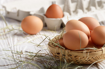 Raw organic brown chicken eggs in square wicker basket on white kitchen wooden table