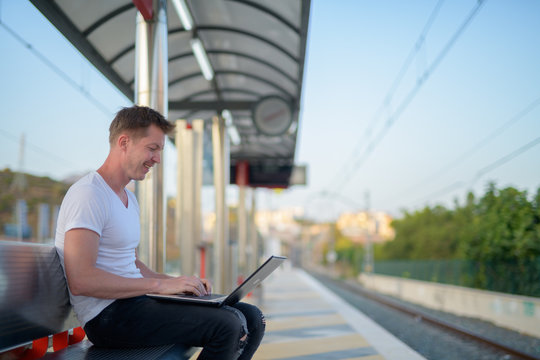 Profile View Of Young Happy Tourist Man Using Laptop At The Train Station