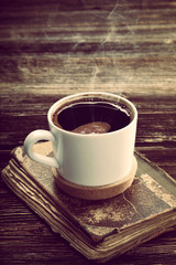 Old book and cup of coffee on vintage wooden background