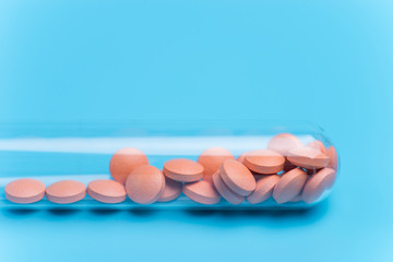 Orange pills or tablets drop out of the test tube on blue background