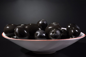 Bowl of black olives against a dark background.