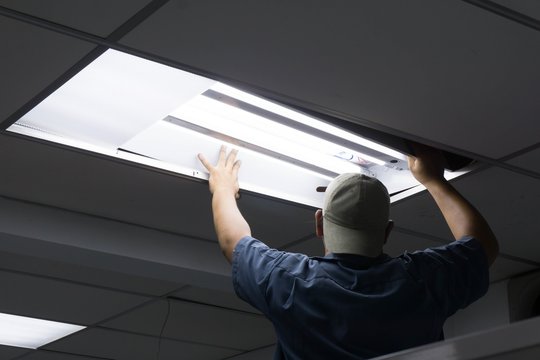 The man checking or changing Fluorescent light tube in the building.