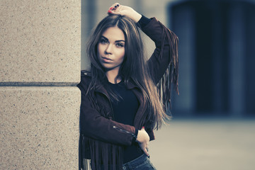 Young fashion woman in leather fringe suede jacket leaning on the wall