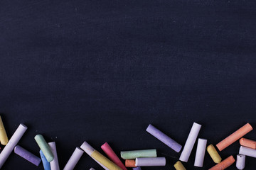 Multicolored crayons lie on a black chalkboard, copy space. The concept of school, education and...