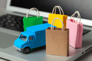 Delivery of orders from the online store. Shopping bags in shopping cart on laptop keyboard and courier delivery truck