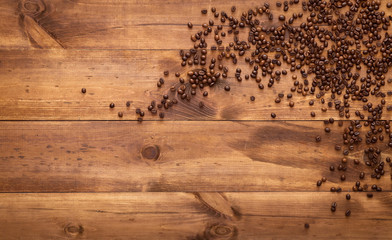 Black coffee beans seed scattered on brown wooden table, dark cofee espresso roasted grain flavour aroma cafe, natural coffe shop background, top close up view from above, flat lay, copy space