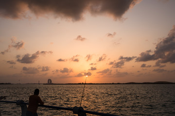 A man fishing while watching Sunset at Corniche beach during heavy dark clouds