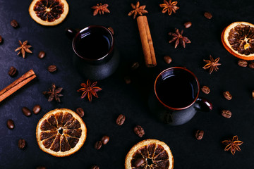 A cup of coffee, star anise, cinnamon, dried orange and coffee beans on a dark kitchen countertop. Fragrant spices for a drink, close-up, top view, flat ley.