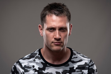 Fototapeta premium Dramatic moody close up portrait of angry young adult man with intense staring at camera on gray background. 